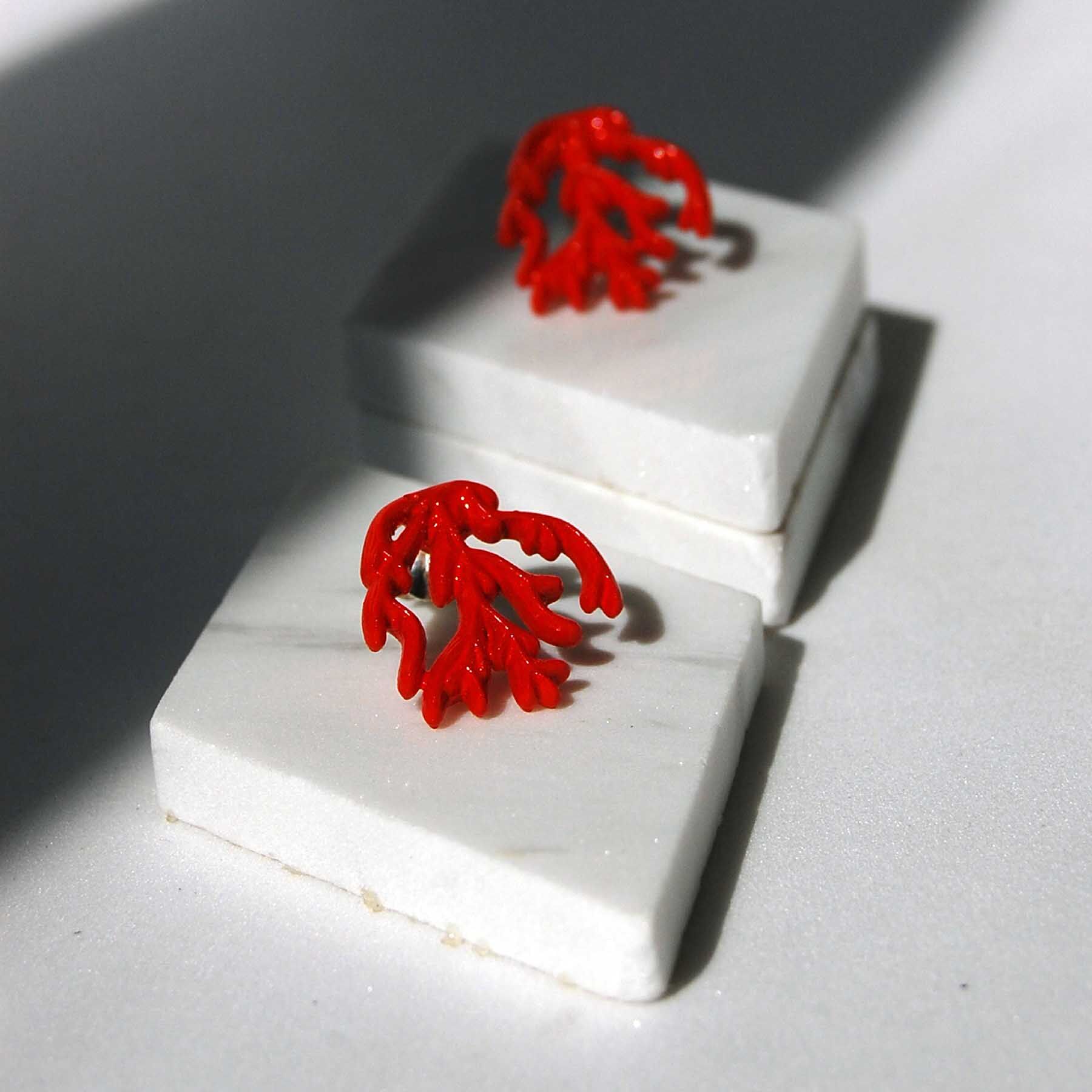 pendientes con forma de colar, color rojo sobre baldosa de marmol blanco y fondo blanco con sombra pronunciada