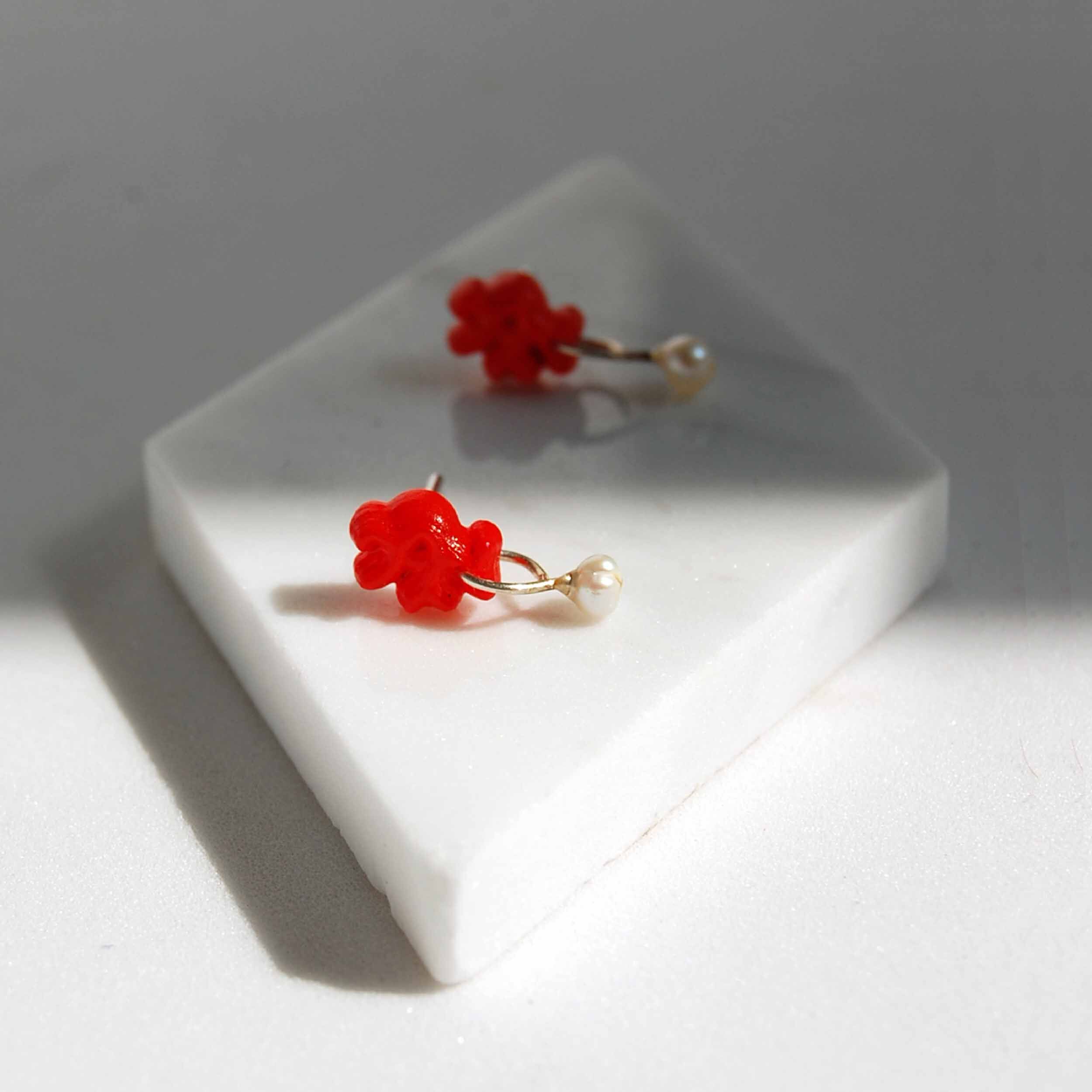 pendientes coral rojo con perla pequeños sobre baldosa rombo de marmol blanco