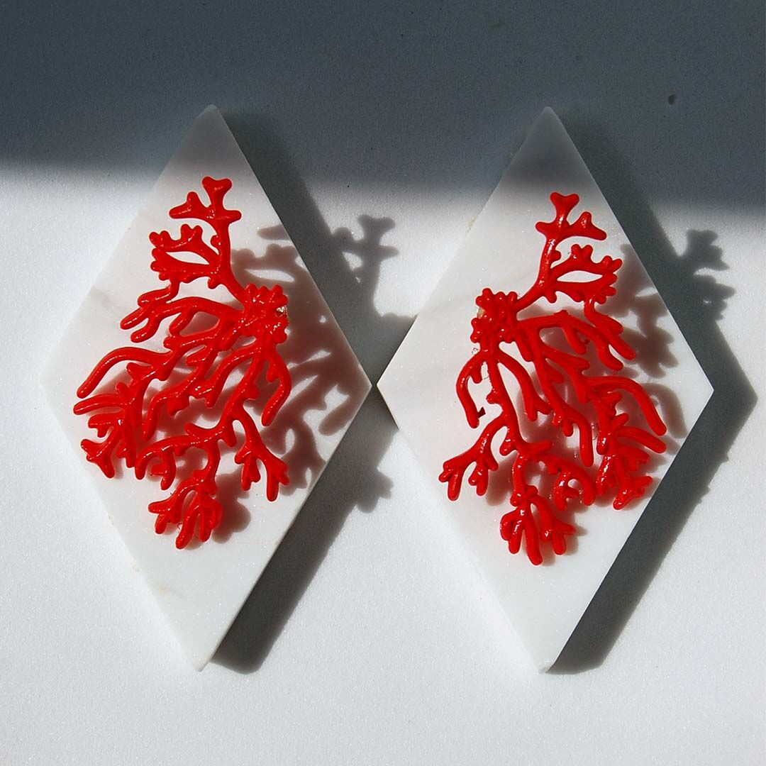 Pendientes con forma de coral rojo impresos en 3d sobre baldosa de marmol romboide blanco entre sol y sombra